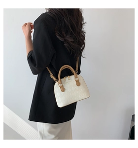Detail of minimalist shell bag featuring beige quilted texture and brown leather handles
