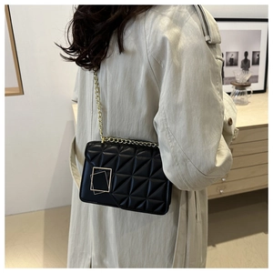 Détail du sac bandoulière matelassé noir avec chaîne dorée sur un trench