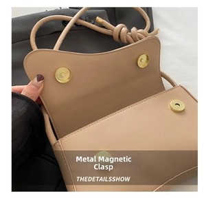 Close-up of beige leather bag featuring dual pale gold magnetic snap closures and knot strap