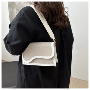 Detail of canvas shoulder bag with wave-curve flap and wide white adjustable strap