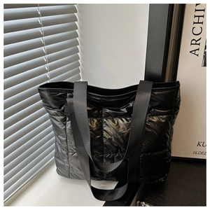 Detail shot of black quilted tote bag with glossy nylon fabric on a dark wood surface