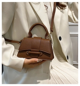 Close-up of brown litchi leather handbag with trapezoid design and metal buckle
