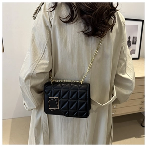 Sac à bandoulière noir matelassé avec chaîne dorée porté élégamment sur un trench-coat