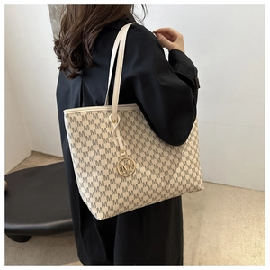 Detail of off-white tote bag with M-pattern monogram and gold metal charm pendant