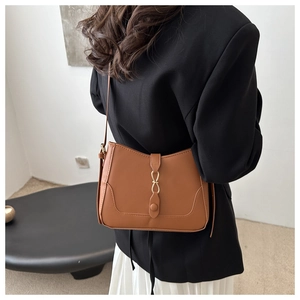 Borsa a spalla in pelle marrone indossata con blazer nero e gonna a pieghe su modella