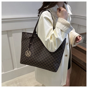 Close-up of brown monogram tote bag featuring golden M pendant and leather straps