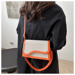 Detail of canvas and orange leather patchwork bag featuring a wave-edge flap design