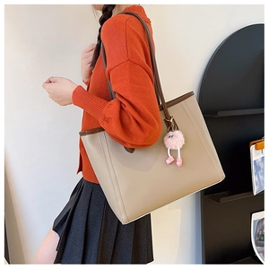 Close-up of beige tote bag with brown straps and pink plush ball charm on shoulder