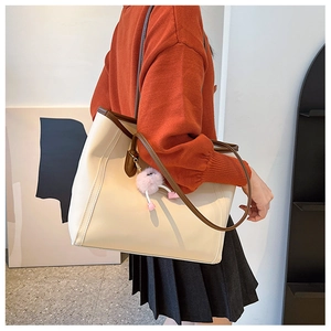 Close-up of beige tote bag with brown leather trim and a pink plush pom-pom charm