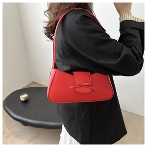 Detail of red glossy baguette bag featuring a stylish bow and smooth leather texture