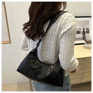 Gros plan d'un sac hobo minimaliste en similicuir noir porté à l'épaule avec bandoulière réglable