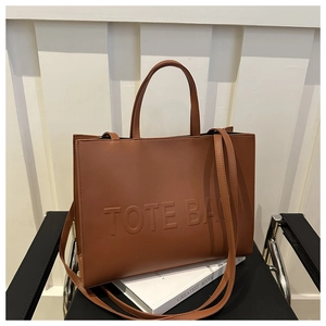 Stylish brown faux leather tote bag with embossed lettering on a modern black chair