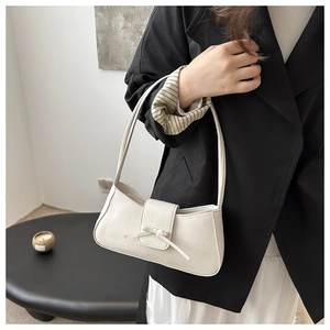 Detail of a creamy white baguette bag with a decorative bow and soft PU leather texture