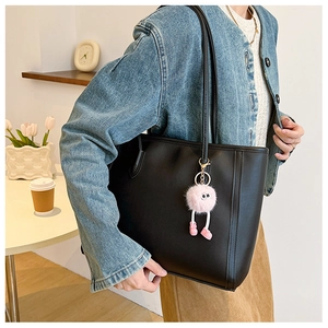Black leather tote bag with pink plush monster charm shown in a cozy indoor setting