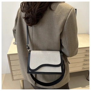 Detail view of canvas shoulder bag with black leather trim and wavy flap design on model