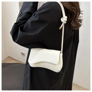 Side view of a white flap shoulder bag with unique wavy bottom and knotted strap detail