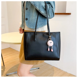 Detail of a black leather tote bag with stylish pink plush charm on shoulder straps