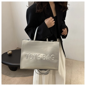 Detail shot of a silver metallic tote bag with embossed letters and adjustable strap