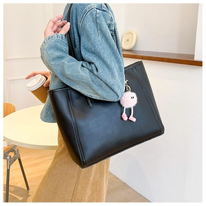 Side view of black matte tote bag with pink fur charm on a model's shoulder for casual commute