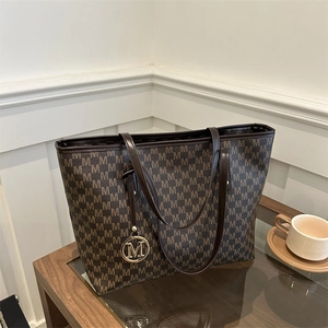 Brown monogram tote bag with gold M pendant on a side table for commute style
