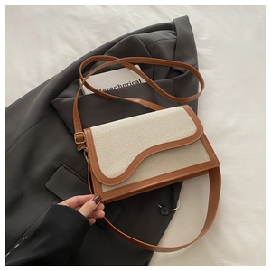 Detail of minimalist beige fabric and brown leather patchwork bag with wavy flap design