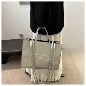 Detail of silver metallic tote bag with embossed TOTE BAG lettering and sturdy handles
