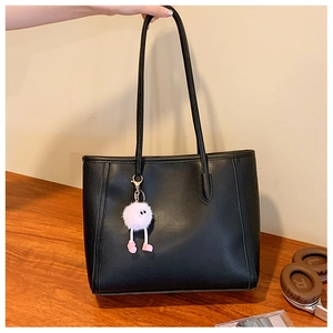 Detail of black leather tote bag with a cute pink pom-pom charm held by hand