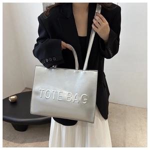 Detail of silver tote bag with embossed logo and textured metallic finish on shoulder