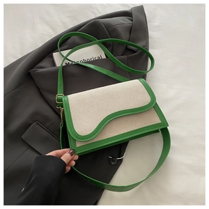 Detail of a chic green and cream patchwork shoulder bag on a grey blazer backdrop