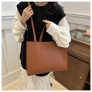 Close-up of the embossed TOTE BAG lettering on a brown PU leather tote bag surface
