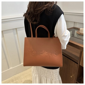 Detail of embossed lettering and leather texture on a large brown tote bag with straps