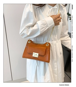 Detail of caramel brown matte leather bag with gold chain strap on white dress