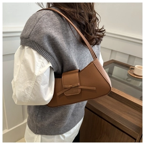 Brown baguette shoulder bag with a bow detail shown worn by a model in a cozy interior