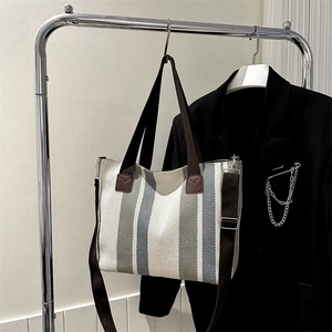 Striped canvas tote bag with adjustable shoulder strap hanging on a metal rack