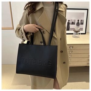 Detail of embossed TOTE BAG lettering on a large black shoulder bag with double straps
