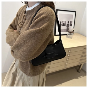 Detail of a black leather baguette bag with bow decoration worn by a model in a cozy room
