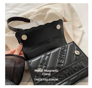 Detail of magnetic closure and embossed FASHION lettering on black crossbody bag