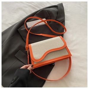 Close-up of stylish contrast canvas bag with orange leather trim and wavy flap design