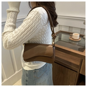 Close-up of brown leather shoulder bag with knotted strap detail and curved bottom design