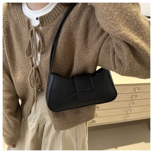 Detail of a black baguette shoulder bag featuring a chic bow and smooth leather texture