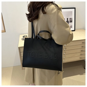 Minimalist black tote bag with embossed lettering on beige trench coat model