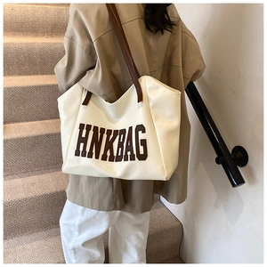 Close-up of cream tote bag featuring HNKBAG letter print and brown shoulder straps