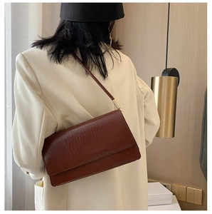 Dettaglio borsa in pelle marrone scuro con trama a coccodrillo e fibbie in metallo oro