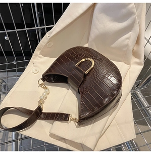 Detail of dark brown croc-effect bag with gold D-buckle and elegant pearl strap accents