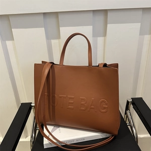 Brown minimalist tote bag with embossed letters on a chair with soft lighting