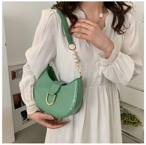 Detail of green crocodile texture saddle bag featuring pearl strap and gold horseshoe buckle