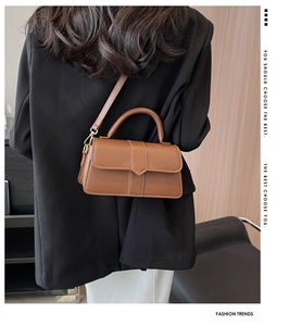 Modern brown leather crossbody bag with V-shaped flap shown on a model's back