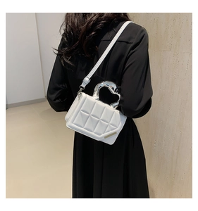 White quilted shoulder bag with silver handle shown on model in modern indoor setting