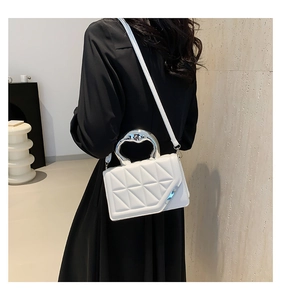 Close-up of a white quilted crossbody bag with a unique silver heart-shaped handle