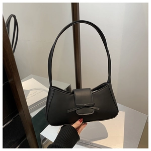 Detail of minimalist black baguette bag with bow clasp and long shoulder strap handle